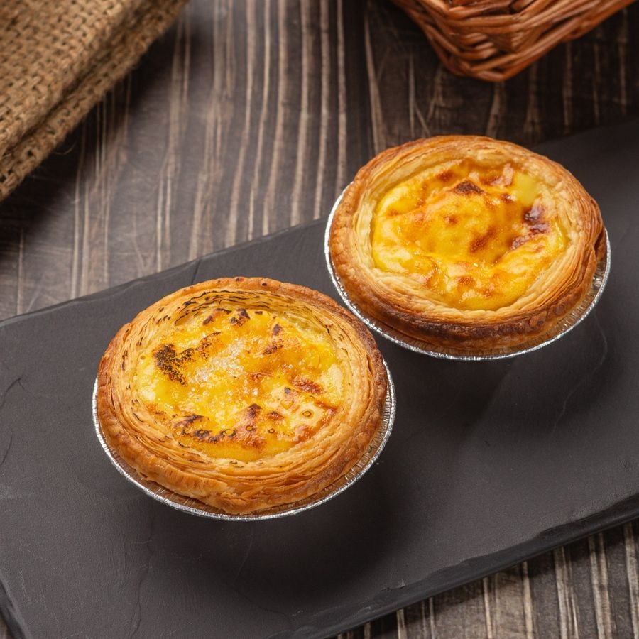 Two Portuguese egg tarts with golden custard on a black tray